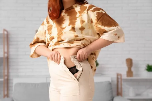 Image of woman trying to do her trousers up after pregnancy weight gain Binley